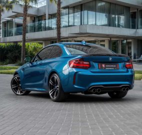 The bmw m2 coupe is parked in front of a modern house.